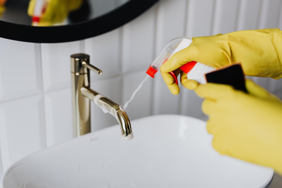 Free From above anonymous housekeeper in yellow rubber gloves spraying cleaner to chrome water faucet in bathroom Stock Photo